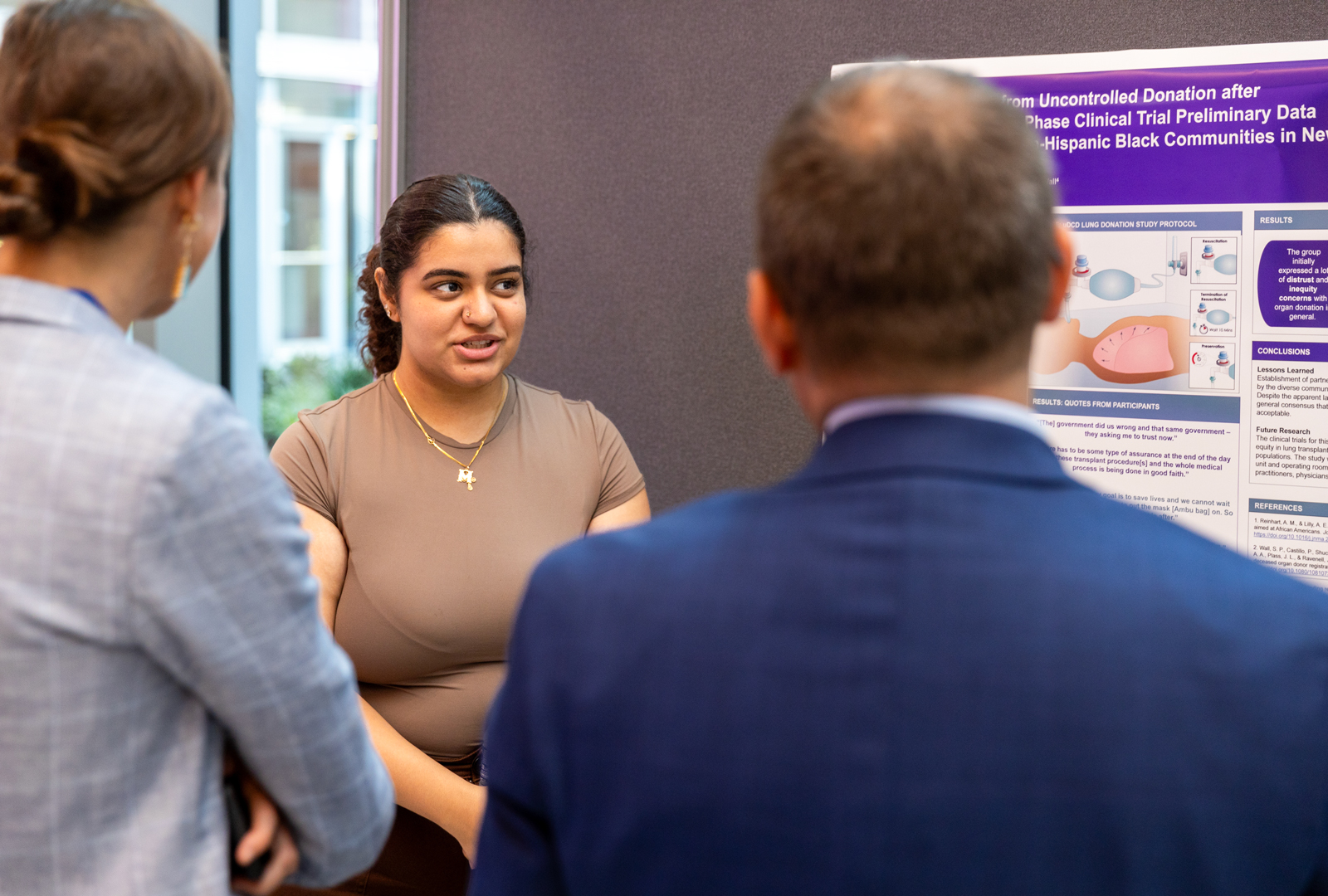 Mariam Girgis speaking with two event attendees about the research on their poster